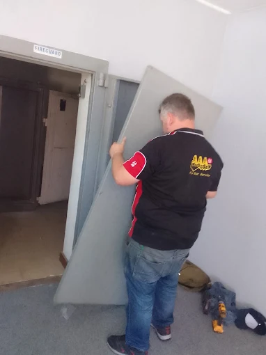 An AAA Locksmiths technician in a branded shirt working on a commercial door